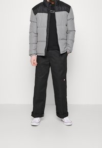 Chaqueta acolchada en gris con una sección superior negra, tela suave, cuello alzado. Combinada con pantalones cargo negros y zapatillas blancas.