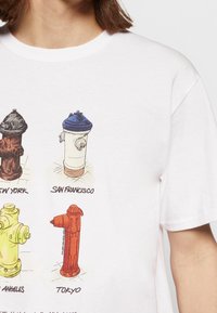 Vit t-shirt med illustrationer av brandhydrant från New York (brun), San Francisco (vit med blått), Los Angeles (gul) och Tokyo (röd).