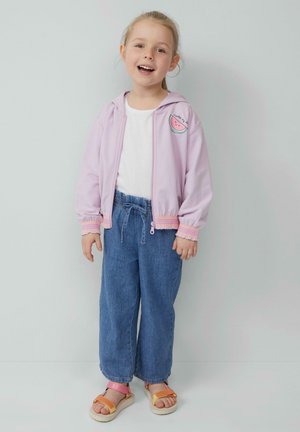 Giacca zip a leggera viola con polsini elastici, decorata con una patch a forma di anguria. Abbinata a pantaloni di denim larghi e sandali con cinturini.