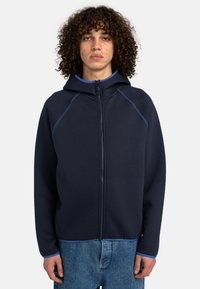 Navy zip-up hoodie with a fitted hood, blue accents, and raglan sleeves. Soft texture and casual fit, paired with light blue interior.