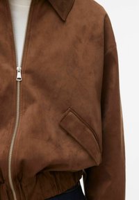 Smeđa bomber jakna od brušene kože s prednjim patentnim zatvaračem, šiljastim ovratnikom, elastičnim strukom i bočnim džepom. Glatka tekstura, ležeran dizajn.