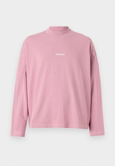 Rozā kokvilnas krekls ar garām piedurknēm un augstu apkakli, ar baltu "BONSAI" logotipu un kontrastējošām šuvēm gar malām.