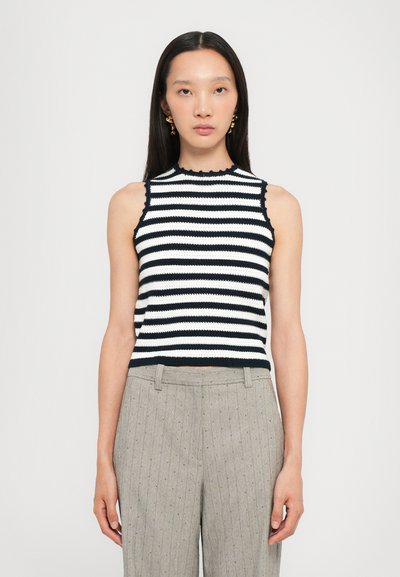 Haut sans manches à rayures noires et blanches avec une texture côtelée, décolleté festonné, porté avec un pantalon à rayures grises claires.