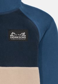 Giacca in pile con un design a blocchi di colore blu navy e beige. Include una toppa logo nera sul petto con grafiche bianche di montagne.