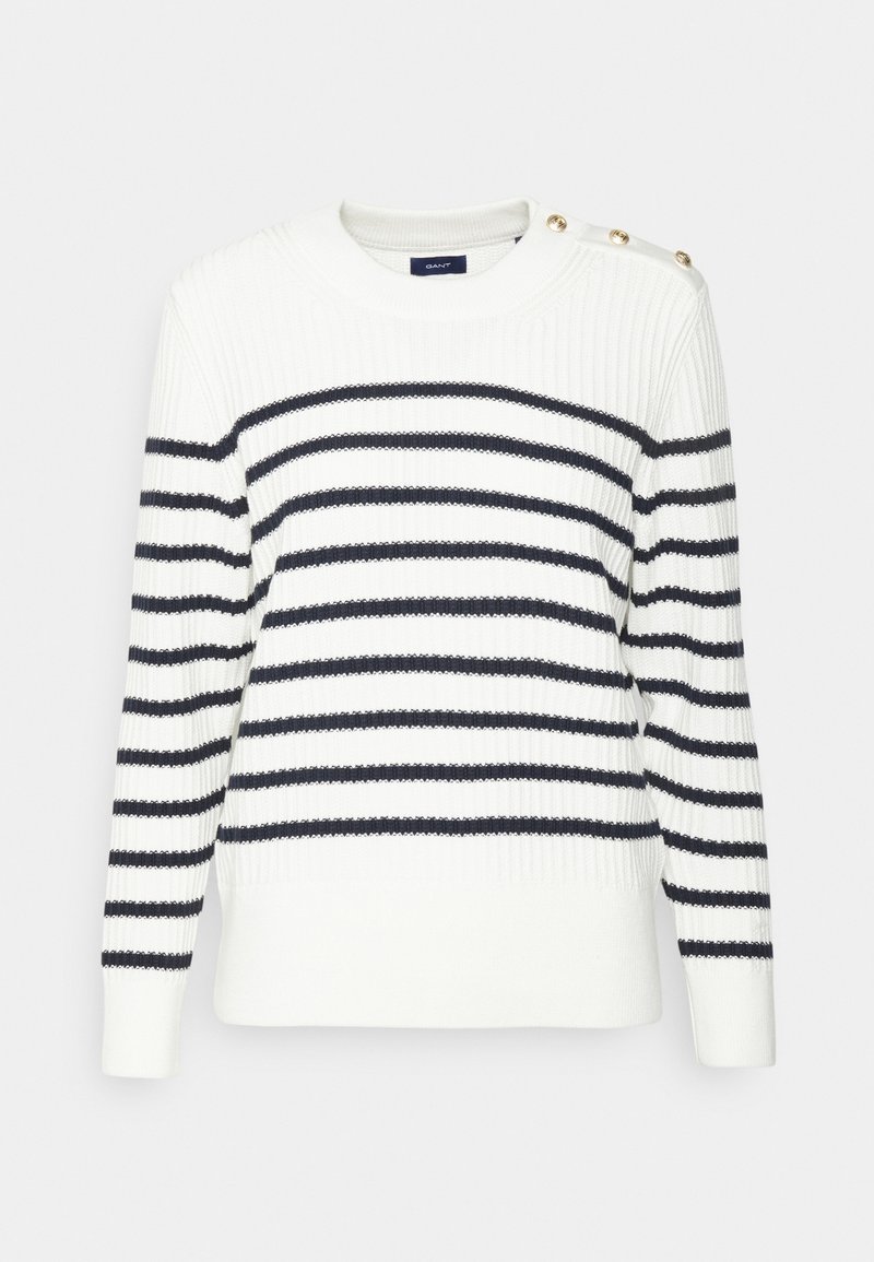 Valkoinen neule, jossa laivastonsiniset vaakaraidat, resorikuvio, pyöreä pääntie ja kultaiset nappikoristeet olkapäällä.