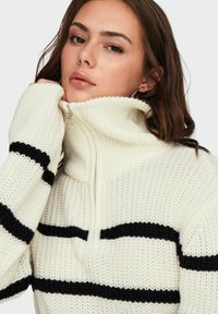 Pull en tricot épais crème avec des rayures horizontales noires. Doté d'un col haut et d'un détail zippé. Tissu texturé avec des poignets côtelés.