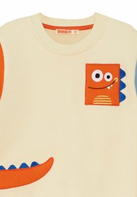 Crème sweatshirt met oranje en blauwe monster appliqués, ronde halslijn en geribbelde manchetten. Etiket leest "DENO KIDS 5Y."