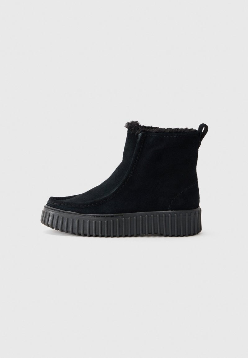 Bottines en daim noir avec une semelle en caoutchouc texturée, un bout arrondi, une doublure en fourrure visible en haut et une languette à l'arrière.