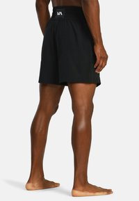 Mannequin staat blootvoets en draagt zwarte sportshorts met het VA-logo op de tailleband, weergegeven van achteren.