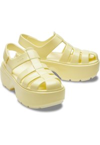 Żółte platformowe sandały o błyszczącej powierzchni, z otwartym przodem i detalami w postaci pasków. Wykonane z lekkiego, elastycznego materiału.
