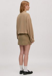 Tan kort trui met verlaagde schouders, gecombineerd met een fitted olijfgroen mini-jurkje met zijsplitten. Zwarte loafers en witte sokken.