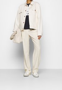 Chaqueta de mezclilla beige, camiseta negra, pantalones de pierna ancha crema y zapatillas blancas. Los accesorios incluyen un bolso beige texturizado.