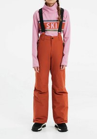 Skiausrüstung bestehend aus einem pinken Langarmshirt mit "SKI"-Schriftzug und orangefarbenen Schneehosen mit verstellbaren schwarzen Trägern sowie schwarzen Schneestiefeln.
