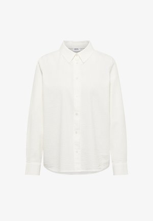 Chemise blanche à manches longues avec boutons, col pointu, tissu texturé et ourlet droit, présentée sur un fond uni.