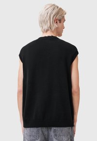 Melns tamborēts bezroku džemperis ar noapaļotu kakla izgriezumu, kam raksturīgas neapstrādātas malas un ērtā piegriezuma siluets, kopā ar gaiši pelēkiem džinsa šortiem.