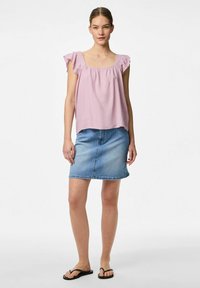 Blusa rosa chiaro a maniche corte con dettagli arricciati; abbinata a una minigonna di jeans in un lavaggio chiaro e sandali neri.