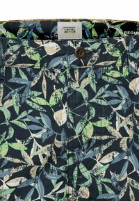 Hochgeschlossene Shorts aus dunkelblauem Stoff mit einem floralem Blättermuster in grünen, beigen und blauen Tönen. Das Etikett trägt die Aufschrift "Camel Active."
