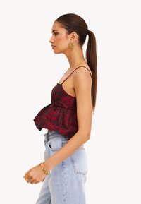 Rode bloemen peplum top met dunne bandjes, gemaakt van een textuurstof. Gecombineerd met lichtblauwe high-waisted jeans en gouden hoepel oorbellen.