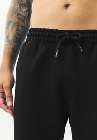Pantalones de chándal negros con cintura elástica y cordón ajustable. La tela parece suave y ligeramente texturizada, adecuada para un uso casual.