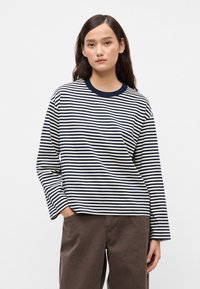 Μακρυμάνικη βαμβακερή μπλούζα ναυτικού και λευκού χρώματος με στρογγυλή λαιμόκοψη και χαλαρή εφαρμογή, συνδυασμένη με καφέ παντελόνι φάρδυ.