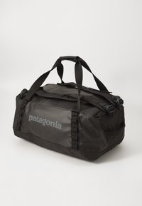 Crni duffel ranac Patagonia s dvostrukim ručkama i naramenicama na bijeloj pozadini, nagnut na desnu stranu.