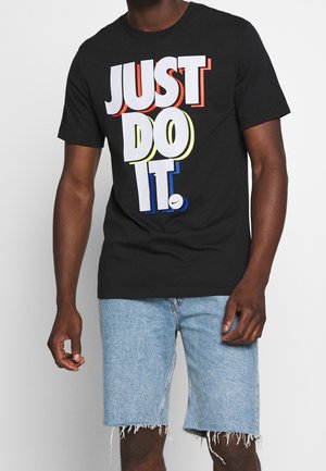 Zwart katoenen T-shirt met de tekst "JUST DO IT." in gedurfde, kleurrijke typografie. Gecombineerd met lichtblauwe denim shorts met rafelige randen.