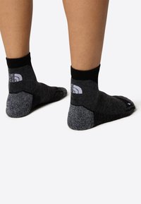 Czarno-szare skarpetki do kostek z teksturowanego materiału, wzmocnioną piętą i palcami, z białym logo z tyłu.