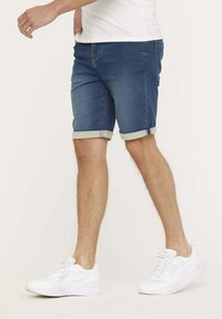 Shorts en denim bleu foncé avec des revers et des coutures contrastantes, associés à des chaussures de sport blanches.
