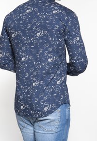 Námořnická modrá košile s dlouhým rukávem se vzorem bílých skvrn, špičatým límečkem a zaobleným lemem. Vyrobena z hladké tkaniny.