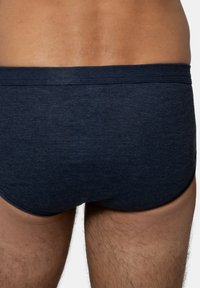 Mörkblå simshorts med ribbad textur, med en låg midjehöjd och elastisk midja. Tyget verkar mjukt och flexibelt.