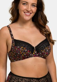 Bralette floral noir avec des bonnets rembourrés, des bordures en dentelle, des bretelles réglables et un nœud décoratif au centre ; motif de fleurs colorées sur un fond foncé.