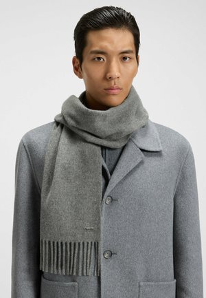 Grå ullscarf med fransdetalj draperad runt halsen, kombinerad med en grå kappa med notched collar och knäppning.