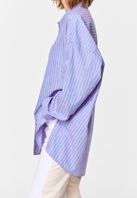 Striped shirt in light blue and pink, with a relaxed fit, long sleeves, a collar, and a single chest pocket. Soft fabric with a smooth texture.