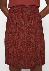 Jupe plissée rouge avec un motif abstrait noir, dotée d'une taille élastique et d'une texture de tissu douce et légère.