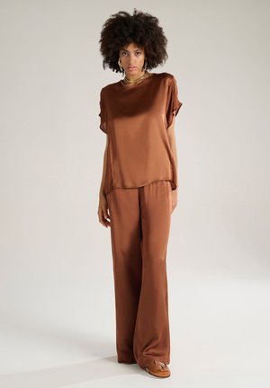 Top in satin marrone con maniche corte e vestibilità ampia, abbinato a pantaloni larghi coordinati. Tessuto liscio, dettagli di design minimi.