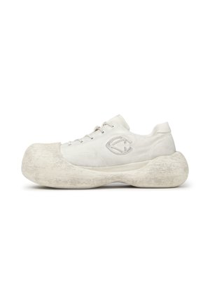 Sneaker bianca con suola oversize e arrotondata e design con lacci, con logo cucito sul lato, mostrata su uno sfondo bianco semplice.