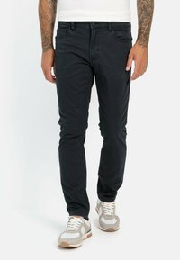 Black denim jeans with a slim fit, five pockets, and a button closure. Worn with grey and white sneakers featuring a textured design.