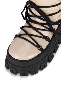 Beżowy pikowany but z połyskującym wykończeniem, czarnym sznurowaniem, grubą czarną gumową podeszwą z wyrazistym bieżnikiem oraz metalowymi oczkami.