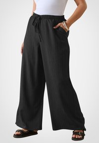 Szerokie czarne spodnie z teksturowanej tkaniny, z elastycznym paskiem w talii i sznurkiem do regulacji. Posiadają dwie boczne kieszenie dla wygody.