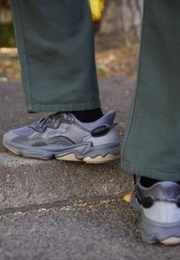 Gray athletic shoes with mesh and synthetic materials, rounded toe, textured sole, and accent detailing on the heel.