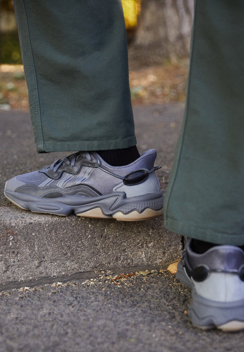 Gray athletic shoes with mesh and synthetic materials, rounded toe, textured sole, and accent detailing on the heel.