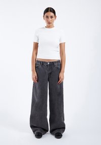 White fitted t-shirt and oversized black denim jeans with a straight-leg design, featuring a button closure and front pockets.