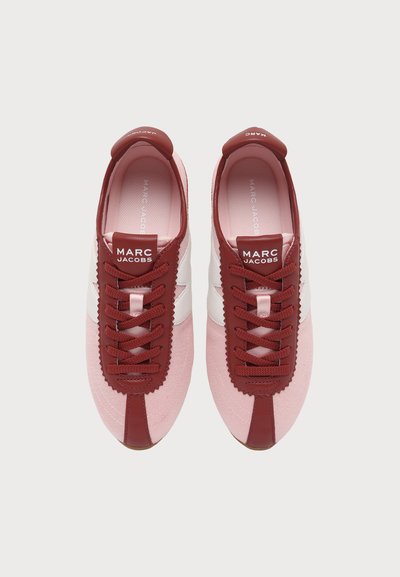 Par ružičastih i bordu Marc Jacobs tenisica s bijelim bočnim detaljima i brendiranim jezičcima, gledano odozgo na svijetloj pozadini.