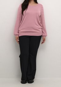 Light pink long-sleeve sweater with ribbed texture on sleeves, paired with black wide-leg trousers and black shoes.