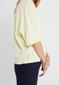 Camiseta oversized color amarillo claro con cuello redondo, mangas cortas enrolladas y un ajuste relajado, combinada con pantalones azul marino oscuros.