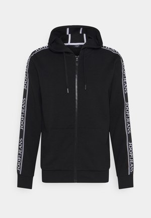 Felpa nera con zip, coulisse e scritta bianca "JOOP! JEANS" sulle strisce lungo le maniche, su uno sfondo semplice.