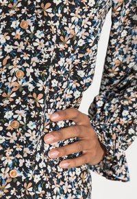 Vestido preto com estampado floral colorido; apresenta fecho de botão e punhos de mangas franzidos. Tecido suave com um padrão texturizado.