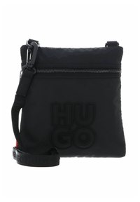 Sac bandoulière noir en tissu texturé, avec une fermeture éclair sur le dessus, un logo embossé et une sangle ajustable. Détails en rouge.