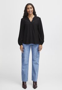 Svart skjorta med knappar och broderade detaljer, långa ärmar, kombinerad med ljusblå cargo jeans med hög midja och mörkbruna ankboots.