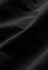 Tissu noir présentant une texture douce avec des plis ondulés et drapés. Le matériau semble lisse et légèrement réfléchissant avec des variations de teinte subtiles.